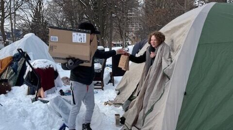 An individual in winter clothing providing direct support and supplies to someone in a snowy outdoor setting