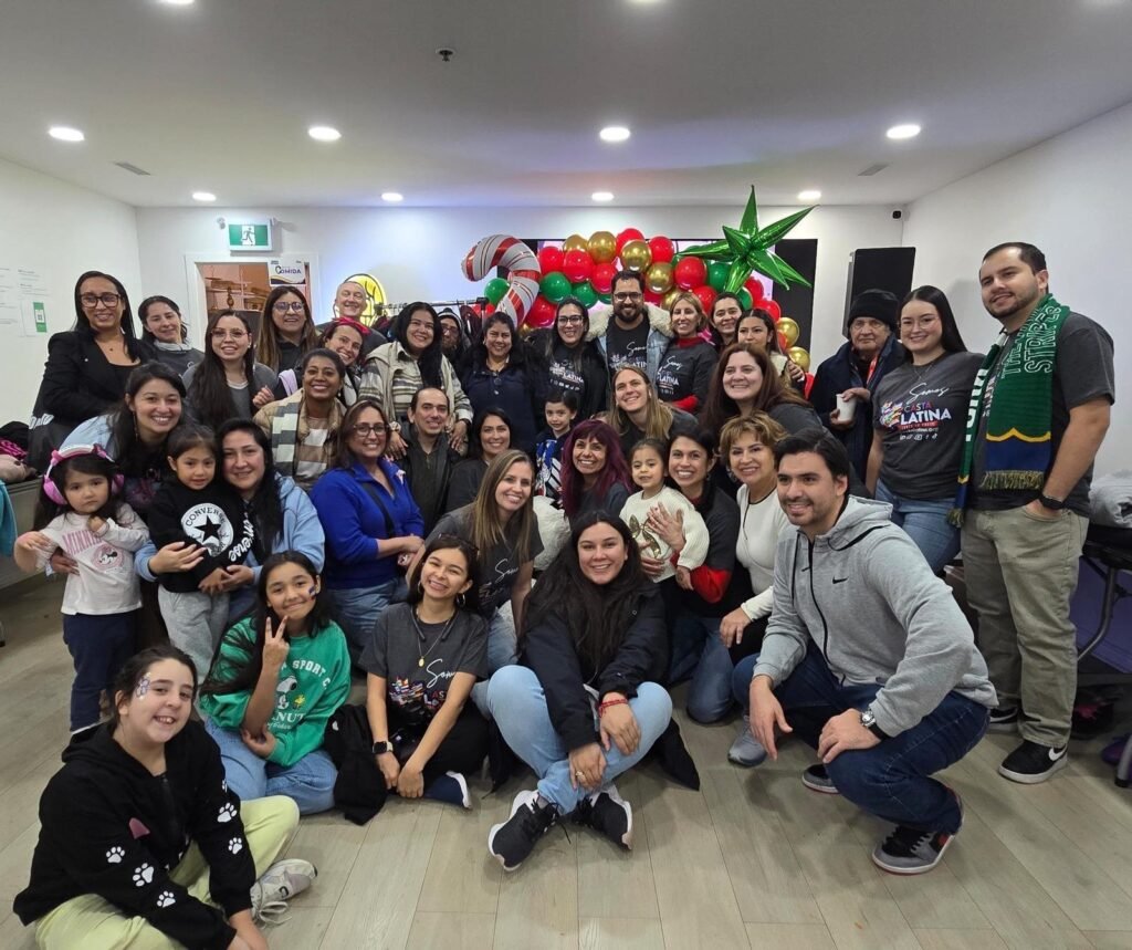 A large, diverse group of adults and children from the Latin American community gathered together, smiling and celebrating.